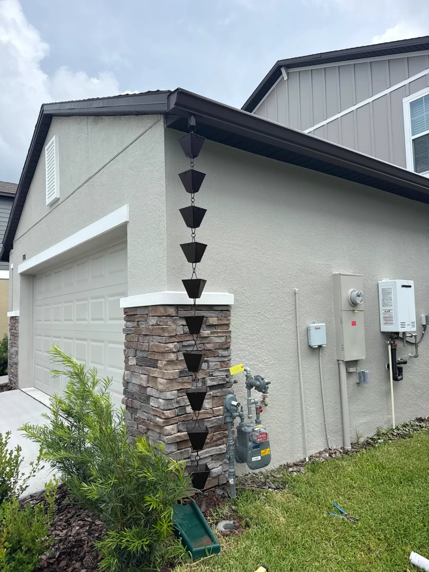 Cup-style rain chain running from the gutter outlet down a stone-faced garage corner column