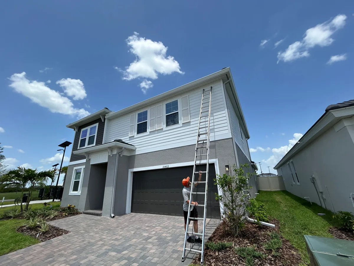 Installer on a ladder beside 7-inch .032-gauge aluminum seamless gutters on a New Port Richey FL home