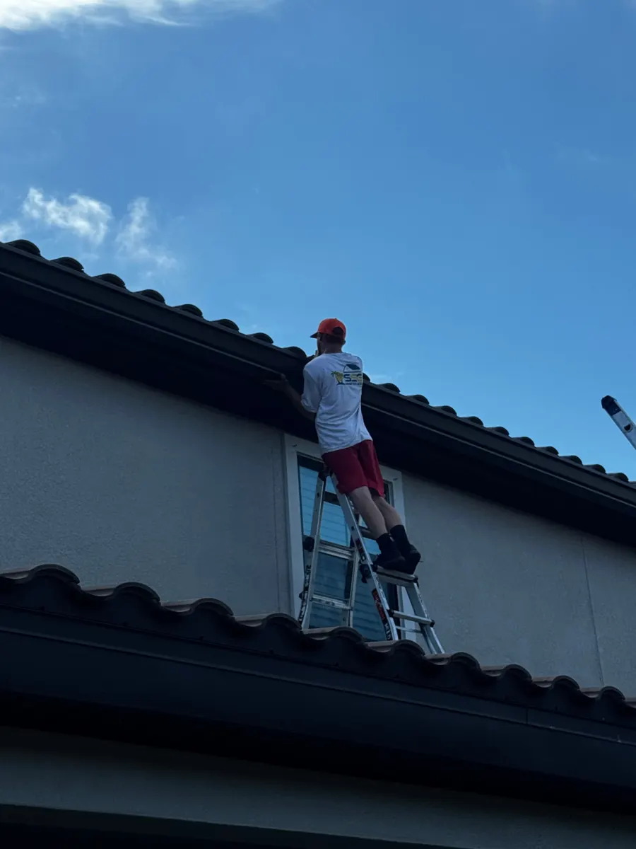 Sunshine State Gutters installer on a ladder working on a dark brown gutter below a tile roof in Starkey Ranch, Odessa FL