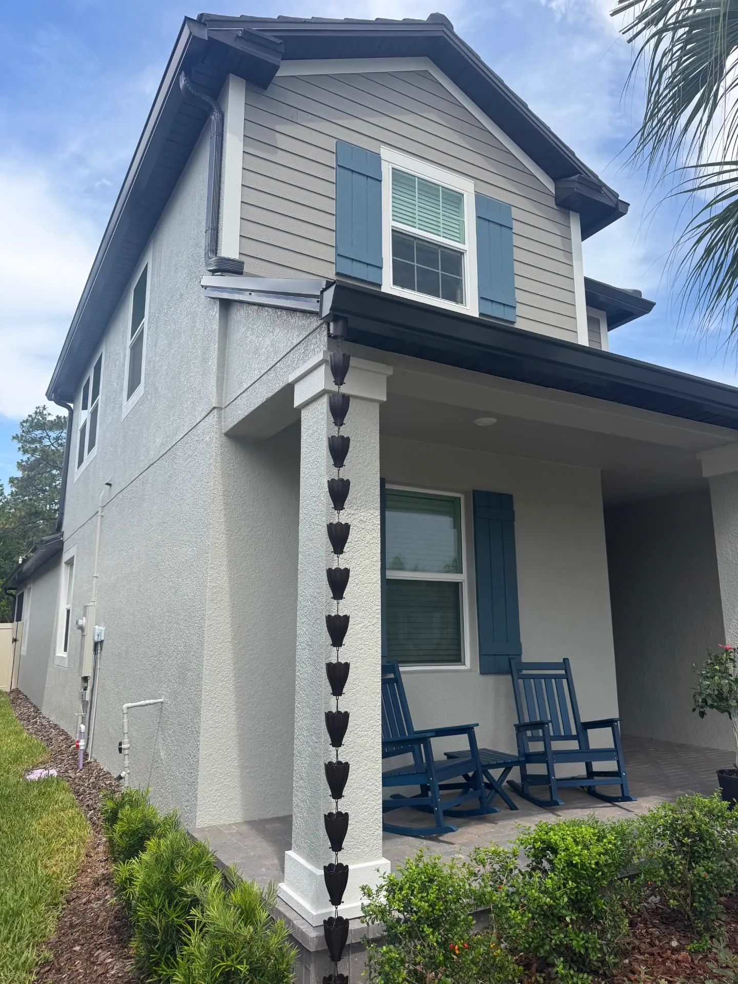 Dark bronze rain chain hanging from a gutter outlet down a porch column of a two-storey Florida home