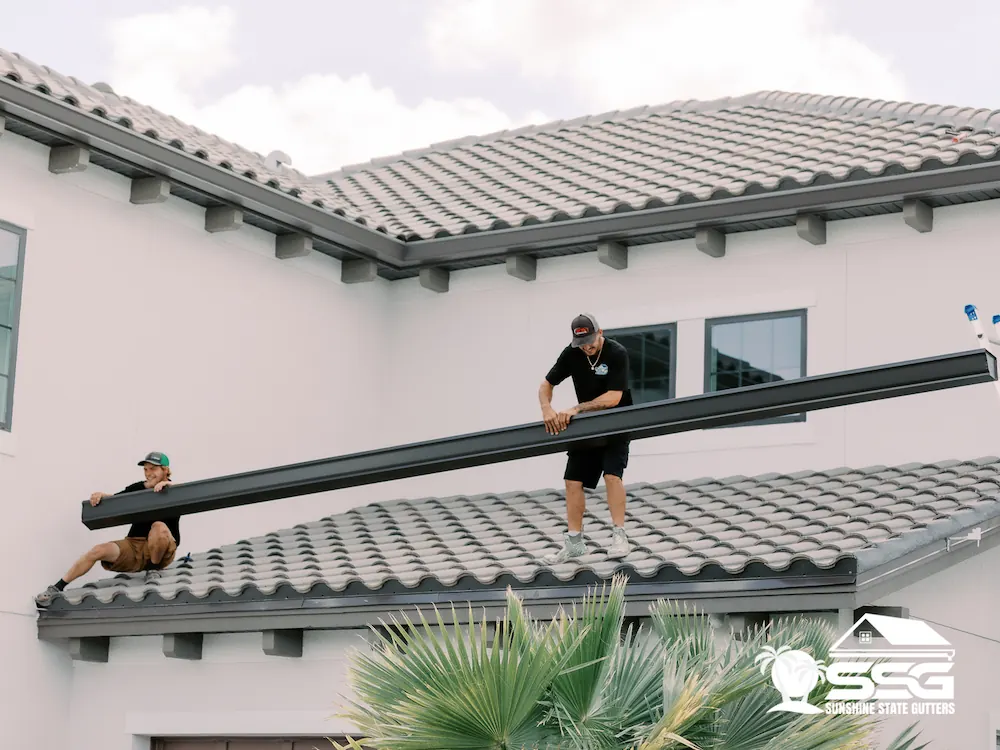 Sunshine State Gutters installers fitting a long seamless gutter on a tile roof home in Florida
