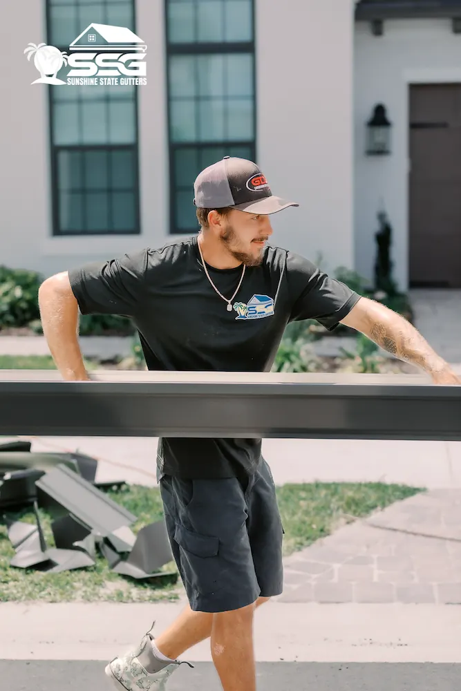 Sunshine State Gutters installer carrying a seamless gutter section during a residential installation.
