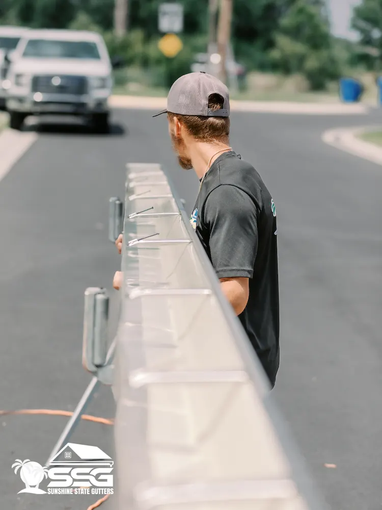 Sunshine State Gutters installer carrying a long seamless gutter section during a residential installation in Tampa, Florida.