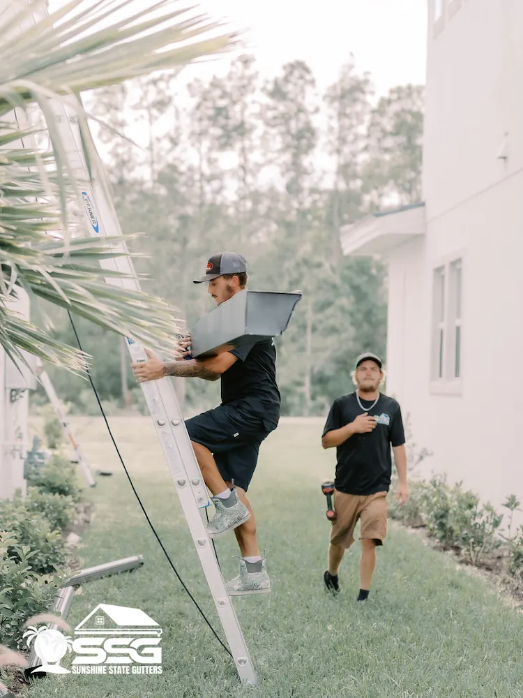 Installer carrying a 7-inch seamless gutter up a ladder on a tile roof home in Florida — Sunshine State Gutters installation team.