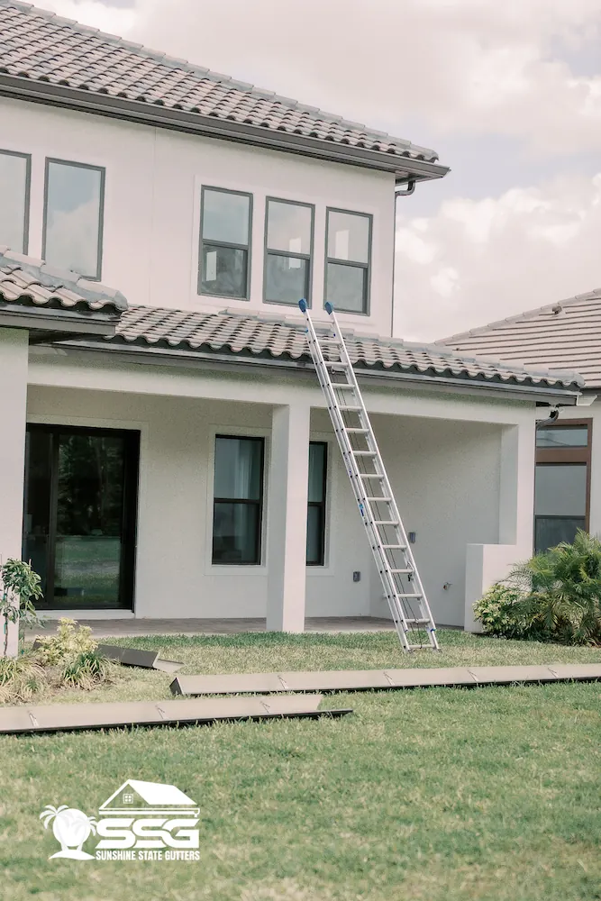 Installer on a ladder working on the gutter line of a tile roof home